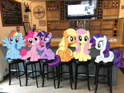 Size: 4032x3024 | Tagged: safe, imported from derpibooru, applejack, fluttershy, pinkie pie, rainbow dash, rarity, twilight sparkle, alicorn, earth pony, pegasus, pony, unicorn, bar, clock, espn, female, grin, head tilt, irl, lake house pub, mane six, mare, michigan, new buffalo, open mouth, photo, photoshop, ponies in real life, sitting, smiling, spread wings, stool, television, wings