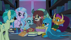 Size: 1280x720 | Tagged: safe, imported from derpibooru, screencap, gallus, ocellus, sandbar, silverstream, smolder, yona, classical hippogriff, dragon, earth pony, griffon, hippogriff, pony, yak, school raze, book, bookshelf, chips, cutie mark, dragoness, female, food, male, smiling, student six, tail, teenager, wings