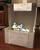 Size: 540x667 | Tagged: safe, artist:nootaz, imported from derpibooru, oc, oc only, oc:nootaz, pony, unicorn, box, cardboard box, cent sign, charlie brown, chibi, cute, female, irl, looking up, lucy van pelt, lucy's advice booth, mare, peeking, photo, ponies in real life, pony in a box, smol, solo