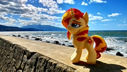 Size: 1200x675 | Tagged: safe, artist:nekokevin, imported from derpibooru, sunset shimmer, pony, unicorn, cloud, female, irl, mare, ocean, photo, plushie, rock, smiling, smug, solo