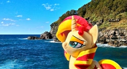 Size: 1199x651 | Tagged: safe, artist:nekokevin, imported from derpibooru, sunset shimmer, pony, unicorn, female, irl, mare, ocean, photo, plushie, rock, smiling, smug, solo