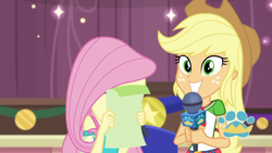 Size: 1920x1080 | Tagged: safe, imported from derpibooru, screencap, applejack, fluttershy, best in show: the pre-show, equestria girls, equestria girls series, spoiler:eqg series (season 2), applejack's hat, belt, best in show logo, clothes, cowboy hat, cute, cutie mark, cutie mark on clothes, denim skirt, duo, duo female, embarrassed, female, geode of super strength, grin, hat, jackabetes, jewelry, magical geodes, microphone, necklace, shy, skirt, smiling