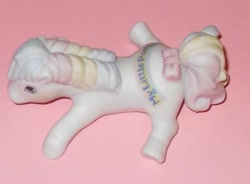 Size: 579x426 | Tagged: safe, imported from derpibooru, photographer:absol, first born, earth pony, pony, adoraborn, bow, cute, female, g1, irl, lying down, mare, multicolored hair, my little pony logo, photo, porcelain, porcelain figurine, prone, rainbow hair, smiling, solo, sploot, tail, tail bow, toy