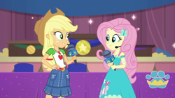 Size: 1000x563 | Tagged: safe, imported from derpibooru, screencap, applejack, fluttershy, best in show: the victory lap, equestria girls, equestria girls series, spoiler:eqg series (season 2), applejack's hat, clothes, cowboy hat, dress, geode of fauna, geode of super strength, hand on hip, hat, looking at each other, magical geodes, microphone, skirt, smiling