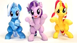 Size: 1024x576 | Tagged: safe, artist:nekokevin, imported from derpibooru, starlight glimmer, sunset shimmer, trixie, pony, unicorn, series:nekokevin's glimmy, bipedal, female, frog (hoof), irl, magical trio, mare, open mouth, photo, plushie, simple background, smiling, trio, underhoof, white background