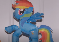 Size: 857x607 | Tagged: safe, imported from derpibooru, screencap, rainbow dash, pegasus, pony, cardboard, cardboard cutout, female, irl, mare, photo, raised hooves, shadow, smiling, solo, youtube link