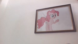 Size: 1280x720 | Tagged: safe, imported from derpibooru, pinkie pie, earth pony, female, hooves, irl, mare, open mouth, paper, photo, picture, picture frame, pointing, smiling, solo, standing, wall