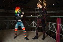 Size: 1280x853 | Tagged: safe, artist:helen the witch, artist:pegasus_fs, imported from derpibooru, rainbow dash, human, armor, boots, clothes, cosplay, costume, glasses, grin, irl, irl human, jacket, leather, leather jacket, looking at each other, looking at someone, photo, rainbow socks, rubronycon, shadowbolts, shadowbolts costume, shoes, smiling, socks, striped socks