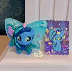 Size: 2841x2785 | Tagged: safe, imported from derpibooru, butterfly, pony, acrylic plastic, book, card, chibi, cutie mark, dinosaw, front view, g5, irl, merchandise, misty brightdawn, official, opaline's dark castle, photo, shaker, window