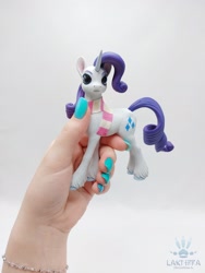 Size: 1620x2160 | Tagged: safe, alternate angle, alternate version, artist:lakterra, imported from derpibooru, rarity, human, pony, unicorn, clothes, craft, female, figurine, hand, holding a pony, horn, irl, mare, photo, polymer clay, scarf, signature, simple background, striped scarf, tail, unshorn fetlocks, white background