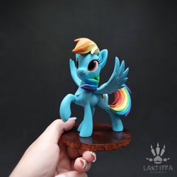 Size: 2560x2560 | Tagged: safe, alternate angle, alternate version, artist:lakterra, imported from derpibooru, rainbow dash, human, pegasus, pony, craft, female, figurine, hand, holding a pony, irl, irl human, looking up, mare, photo, polymer clay, raised hoof, signature, smiling, solo, spread wings, stand, tail, wings